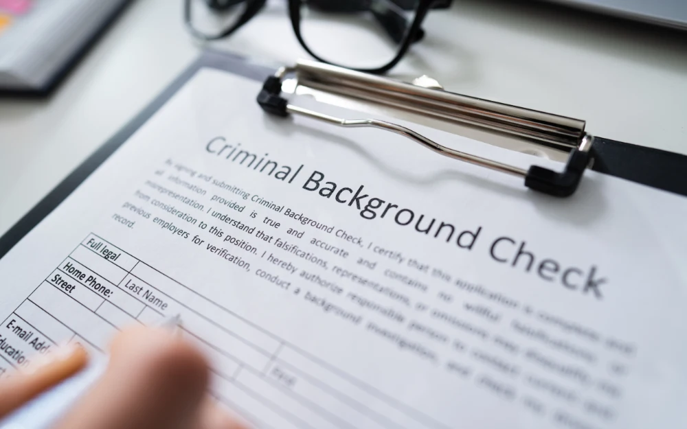 A person's hand filling a criminal background check application form with information such as full legal name and address.