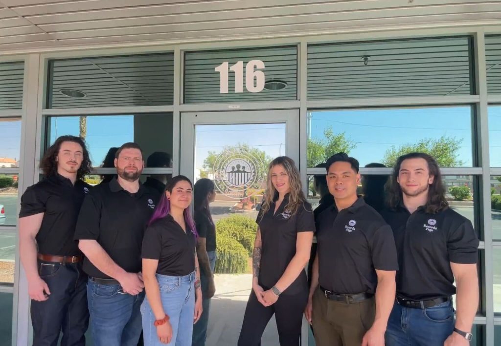 The Records Page team, including Jon, Nathan, and others from the office, are standing in front of a glass door with a decal of the Records Page logo.